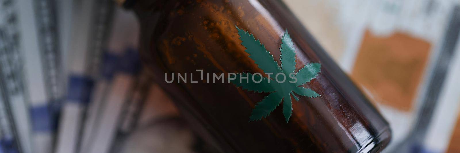 Close-up of glass brown bottle with dropper and cannabis sign lying on money cash. Cannabinoid oil for medical treatment. Narcotic pain relievers concept
