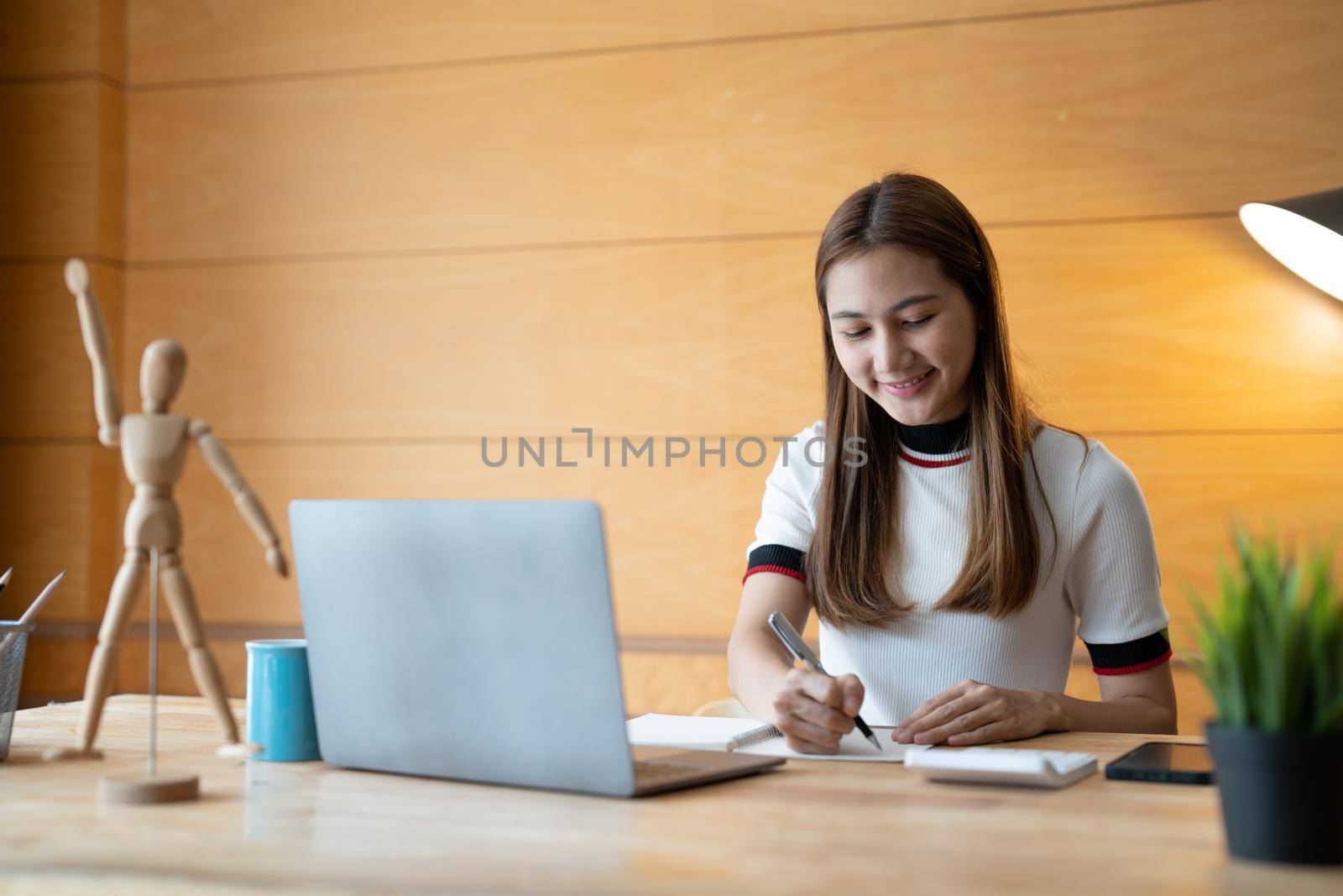 Smiling girl student wear taking note for study online with teacher, happy young woman learn language listen lecture watch webinar write notes look at laptop at home, distant education