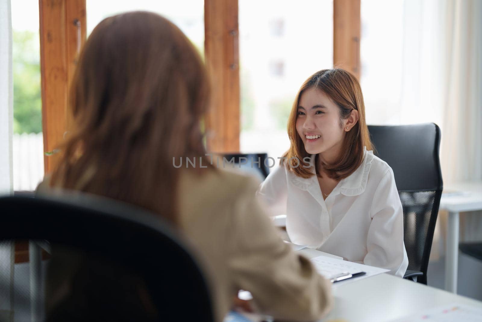 Two young beautiful asian business woman in the conversation, exchanging ideas at modern office