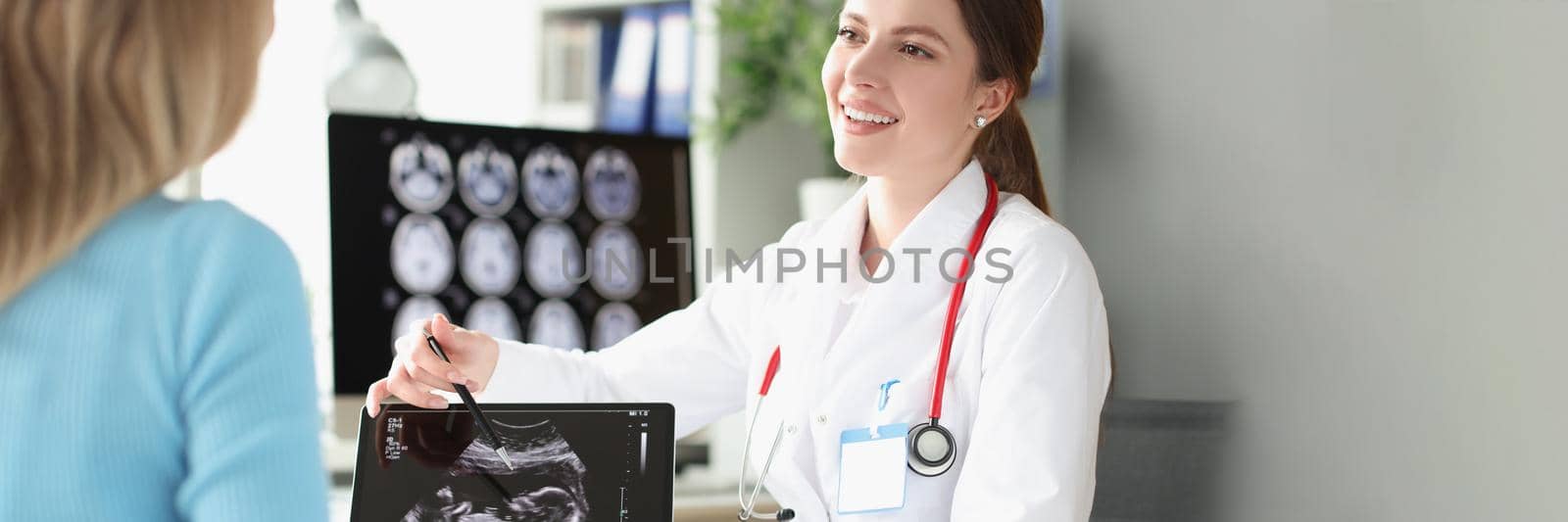 Portrait of smiling gynecologist holding ultrasound picture and showing little child to happy mother. Gynecology, pregnancy and antenatal care concept