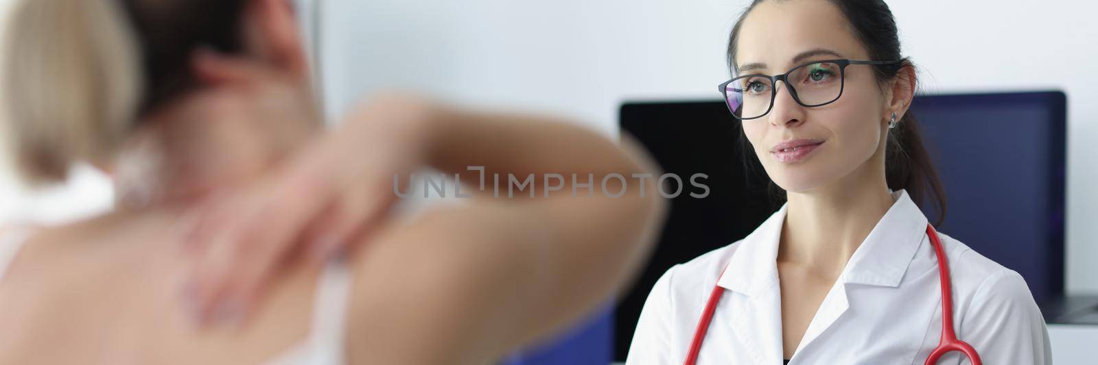 Portrait of cute practitioner examining patient with backache. Surgeon in white gown with stethoscope in clinic office. Treatment, medicine and healthcare concept