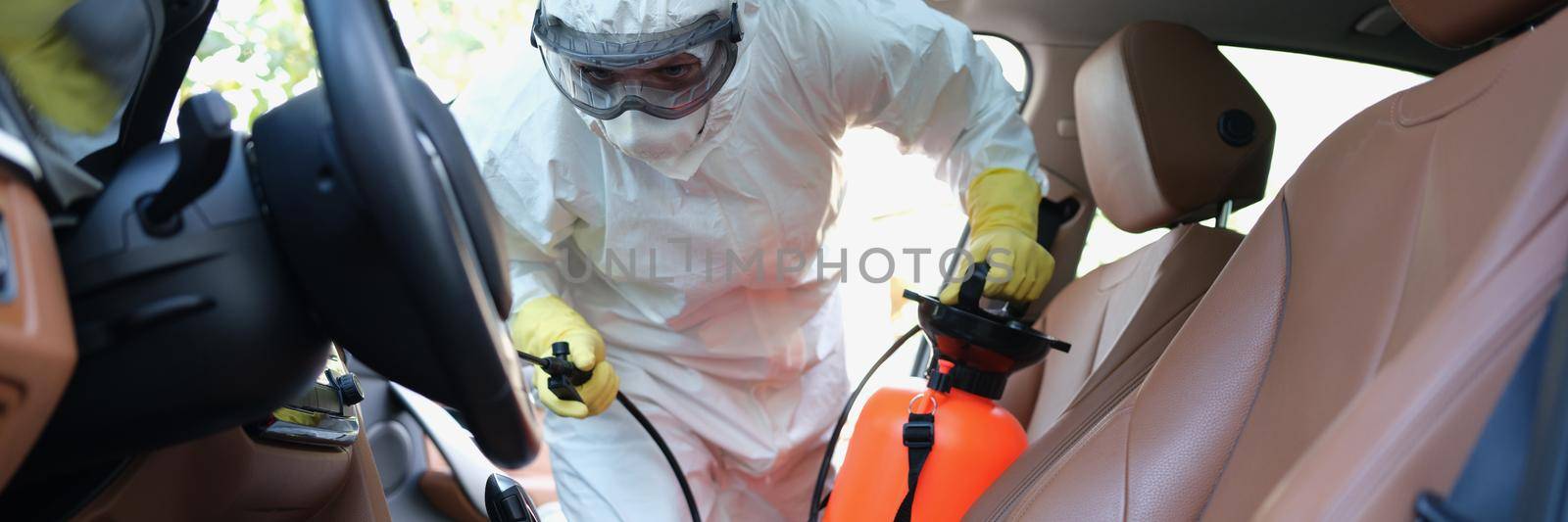 Close-up of male worker cleaning interior of modern car. Team of disinfectors making coronavirus disinfection of vehicle. Worldwide pandemic covid-19 outbreak