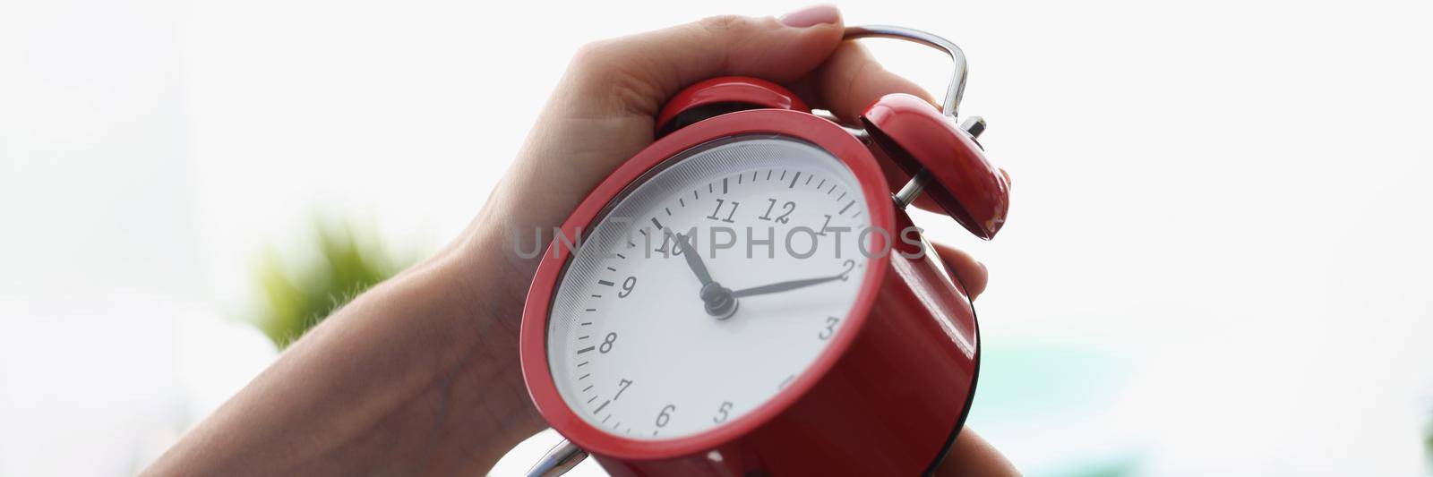 Close-up of woman setting red vintage alarm on proper time, spin arrows on dial, black numbers. Prepare alarm on morning, wake up for work, timer, timepiece concept