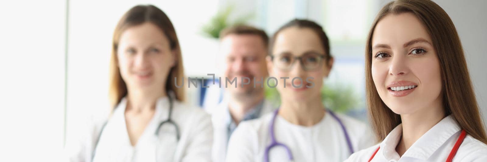 Focus on cute smiling woman therapist posing with colleagues. Physicians in white gowns with stethoscopes. Team of doctors idea. Medicine and healthcare concept