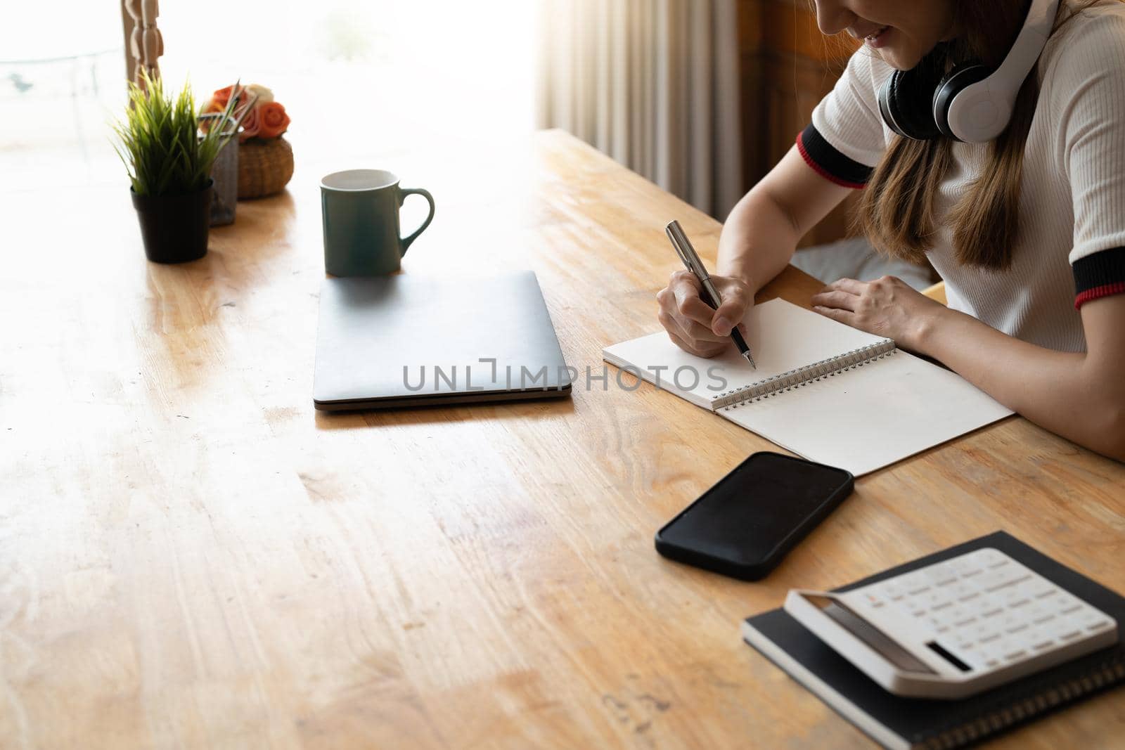 Close up of female hand taking notes in a book with laptop on table. Student studying at home