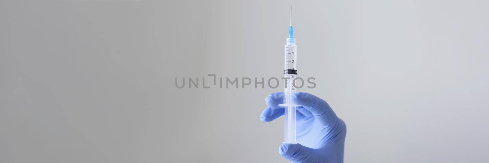 Close-up of person hand holding syringe with transparent substance. Injection, painkiller or vaccination, immunization and treatment concept. Isolated on light background