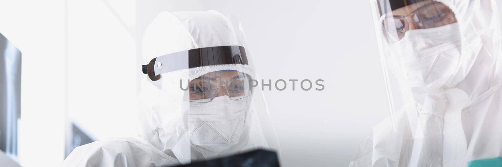 Close-up of therapists in protective medical suits looking carefully at radiograph of sick patient by kuprevich