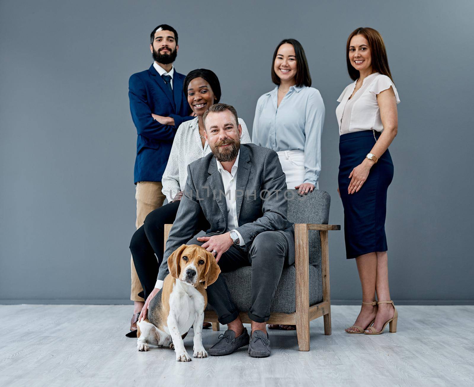 Pets in the workplace reduce stress and nurture productivity. Portrait of a group of businesspeople posing together with a dog against a grey background. by YuriArcurs