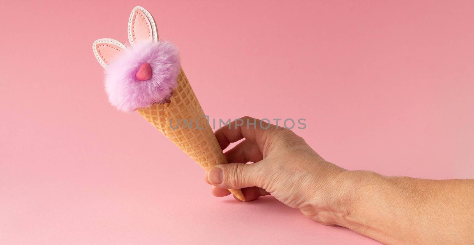 Abstract pink background. A hand with a fluffy lilac rabbit in a waffle cone. The concept of love, a greeting card for Valentine's Day and Easter by lapushka62