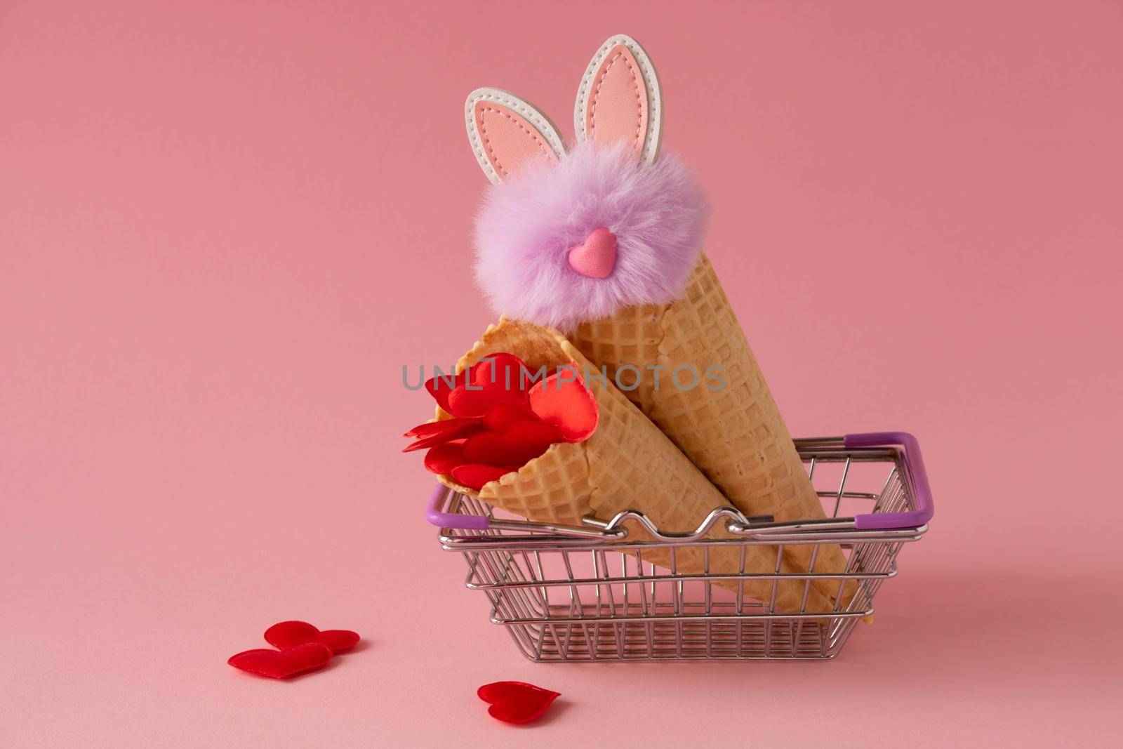 Abstract pink background with red hearts and a fluffy lilac rabbit in a grocery basket and waffle cones. The concept of love, a greeting card for Valentine's Day and Easter. by lapushka62