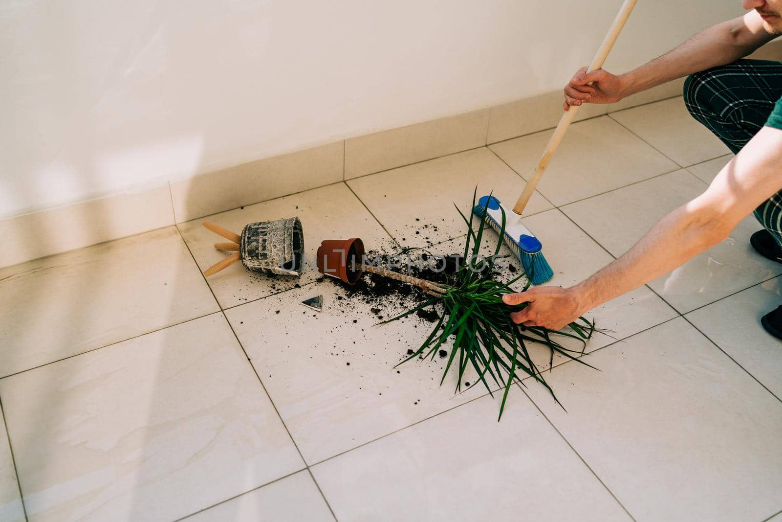 Broken flower pot on the floor with spilled soil and damaged plant. Wiping floor with mop. Home chores - cleaning the dirt. Flower accident with shattered ceramic pot and messy dirt on the balcony.