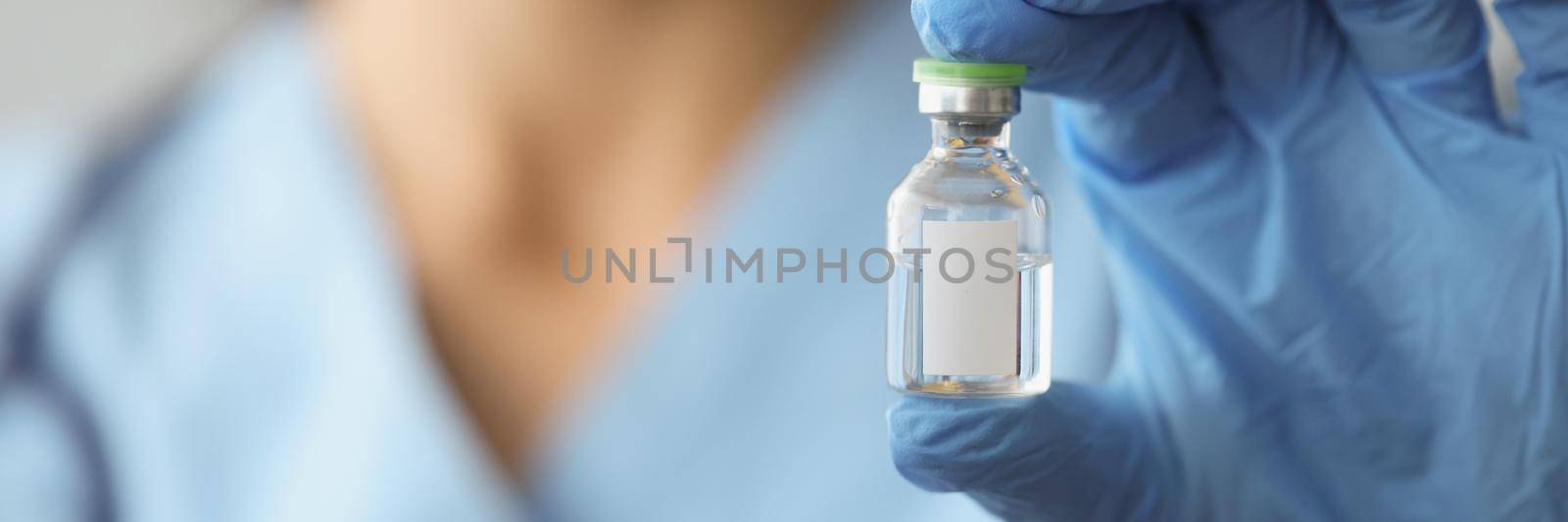 Close-up of doctor hand holding glass bottle with vaccine. Medical ampoule with transparent substance against virus. Vaccination, immunization and coronavirus outbreak concept