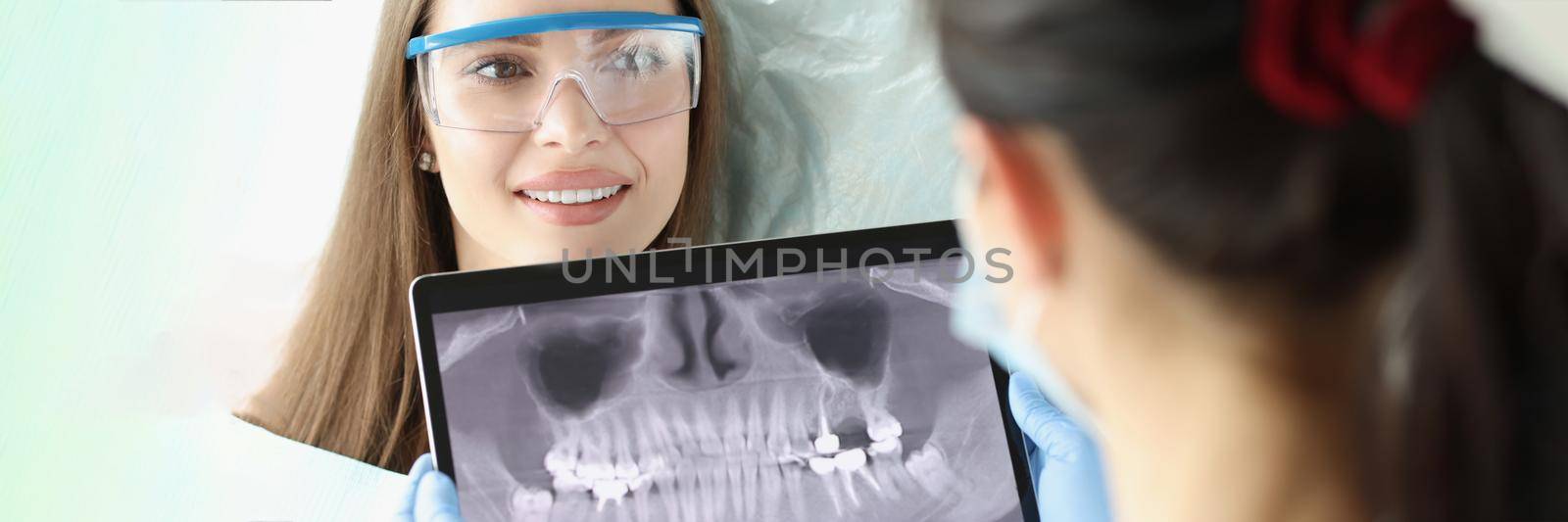 Portrait of cheerful female at dentist appointment. Stomatologist holding dental panoramic X-ray in hands. Dental care, stomatology clinic and healthy teeth concept