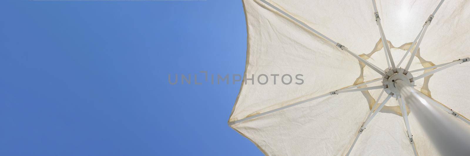 Close-up of white beach parasol, metal stalk and round shaped cover to create shadow from sun. Piece of blue summer sky. Summertime, tourism, holiday, beach equipment concept