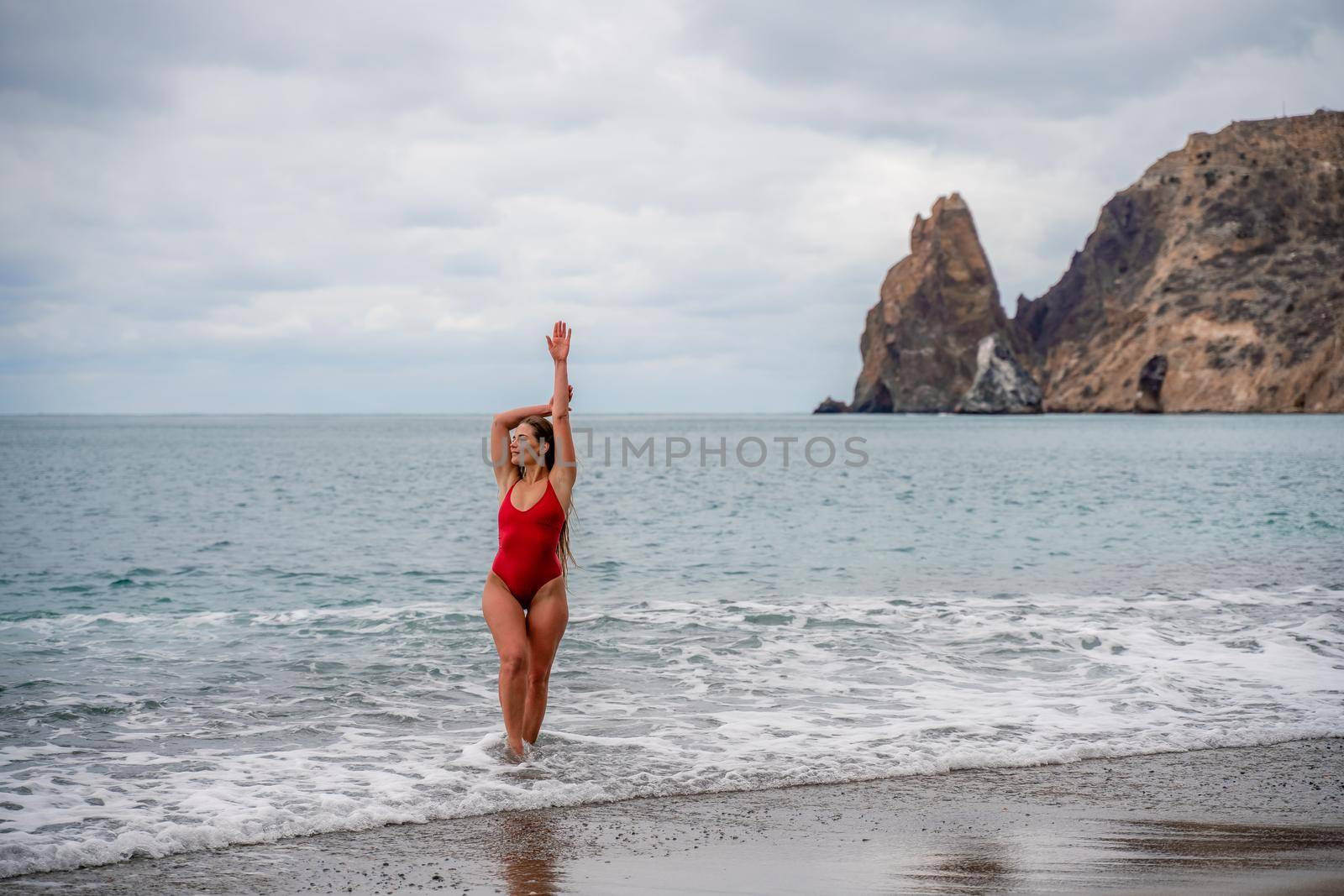 A beautiful and sexy brunette in a red swimsuit on a pebble beach, Running along the shore in the foam of the waves.