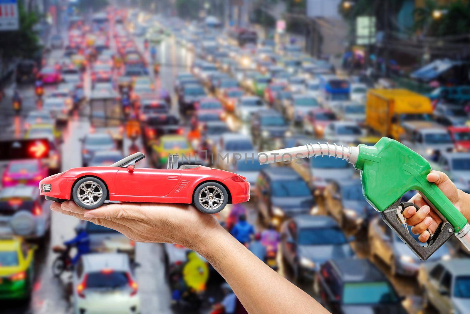 Right hands of men who were holding an automatic nozzle to make refill oil on red toy car on left hand with traffic jam on blurred background. concept idea about industry oil energy