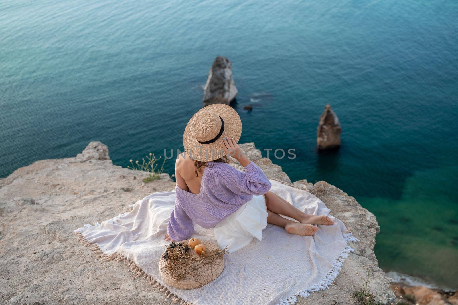 Street photo of a beautiful woman with dark hair in white shorts and a purple sweater having a picnic on a hill overlooking the sea.