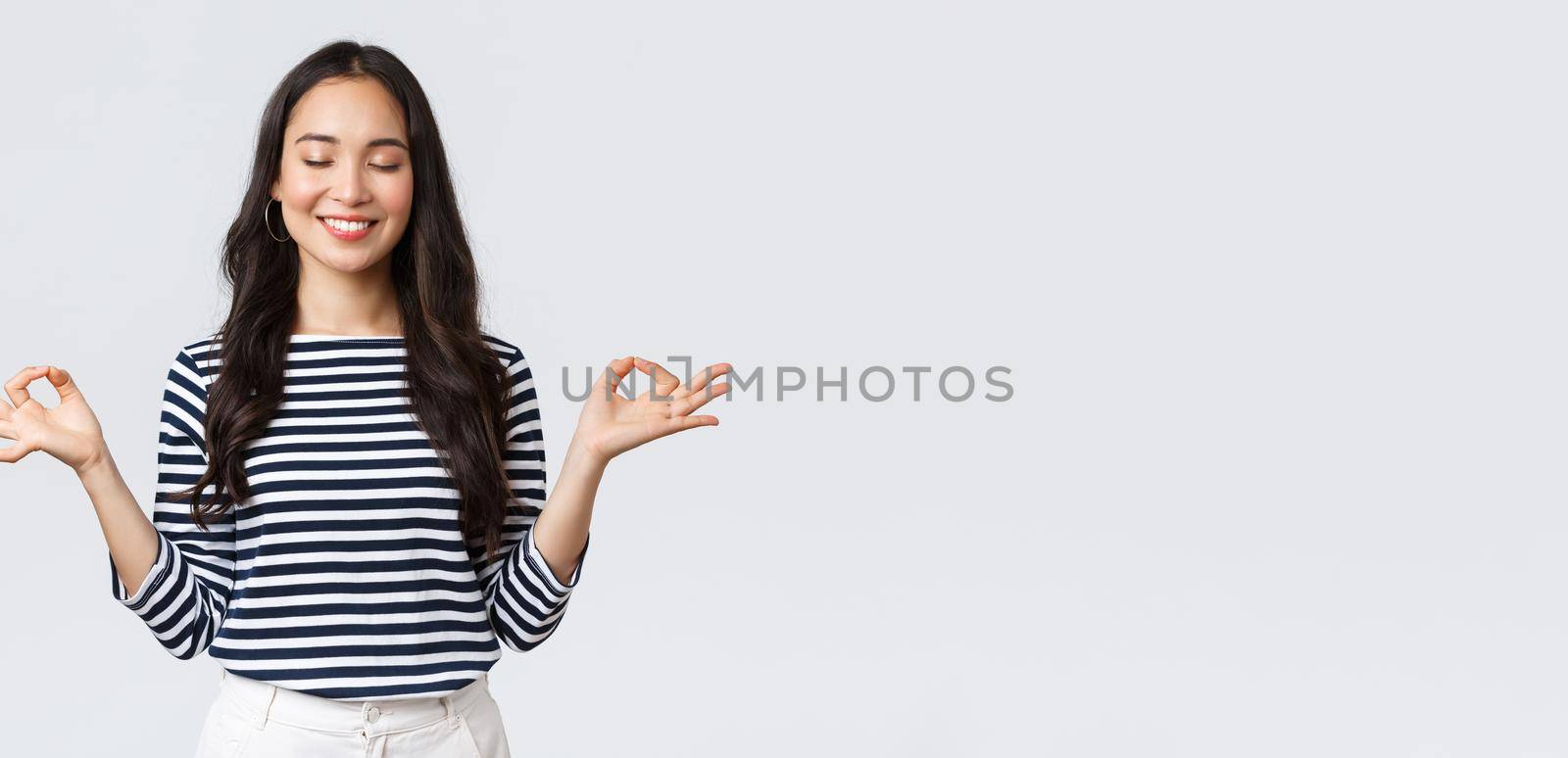 Lifestyle, people emotions and casual concept. Calm happy young woman feeling peaceful during meditation, close eyes and smiling as hold hands in zen nirvana gesture, do yoga exercise by Benzoix