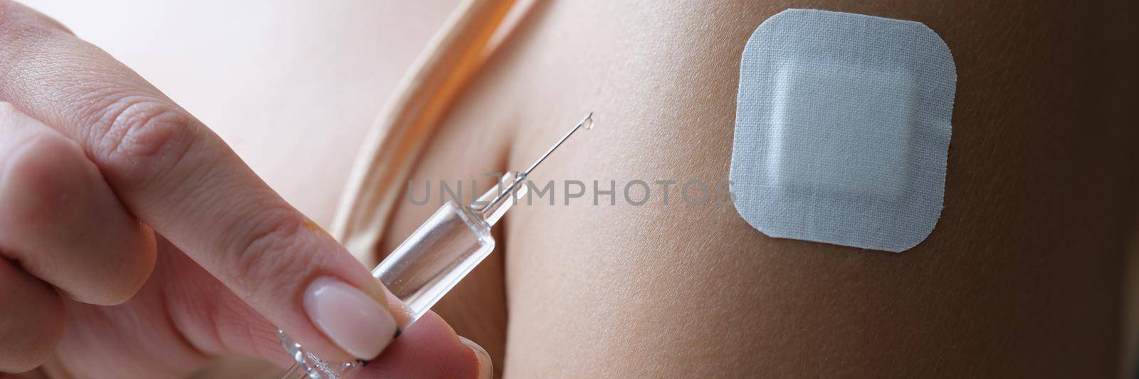 Close-up of female shoulder with patch. Woman holding injection syringe with transparent liquor. Vaccination, immunization against coronavirus and treatment concept