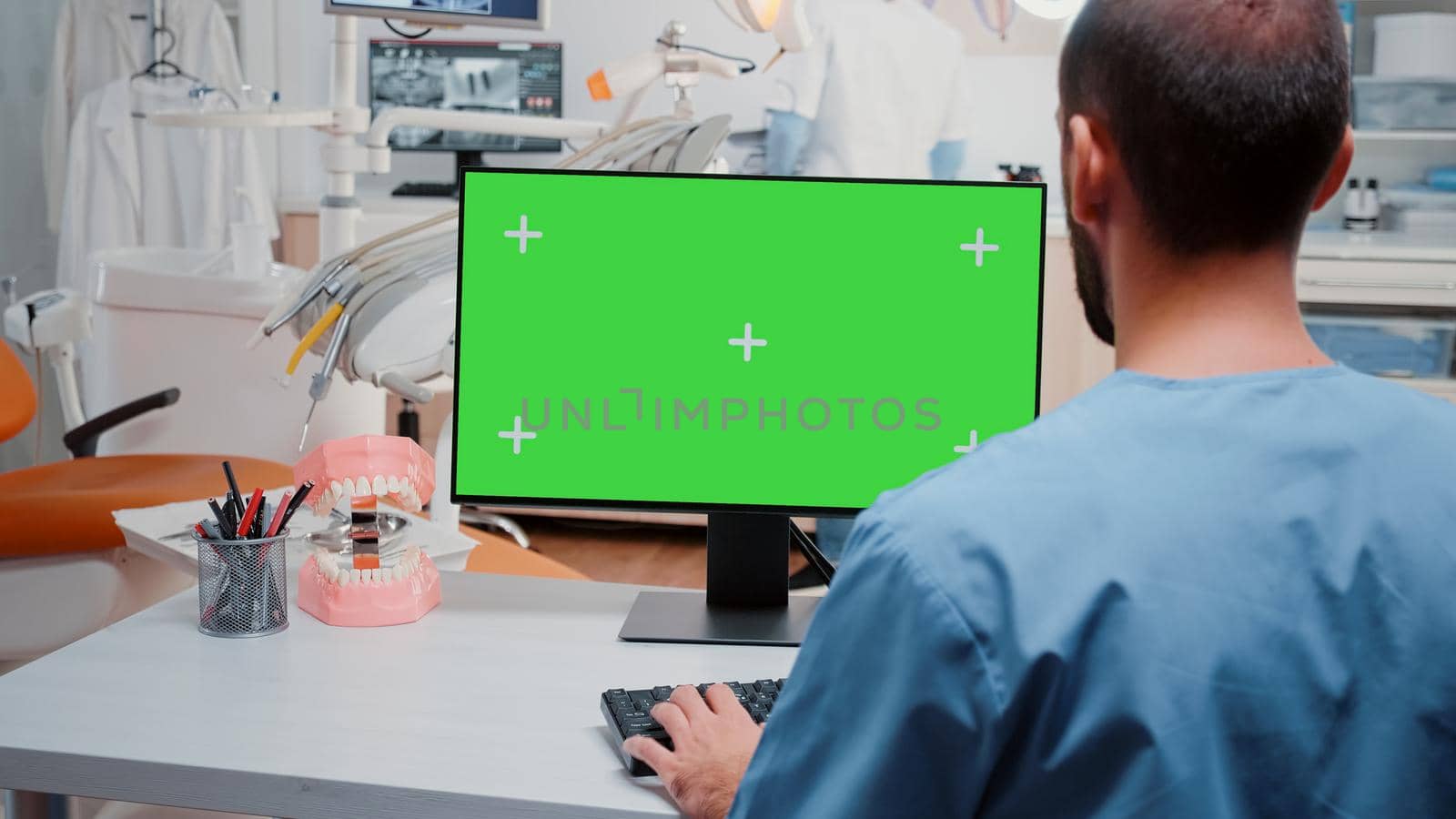 Man looking at computer with horizontal green screen for dentistry at cabinet. Assistant working with chroma key and isolated background on monitor for stomatological care and checkup