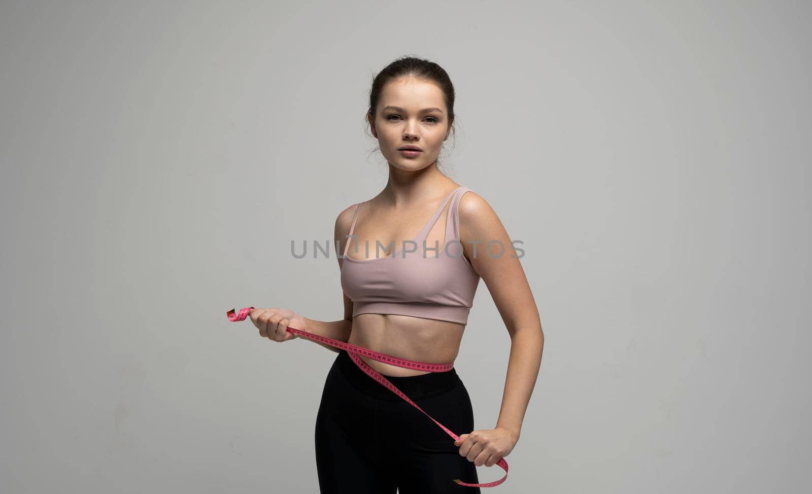 Attractive young brunette women in sportswear and takes measurements of her waist. Measurements of a body. Sport, fitness and diet