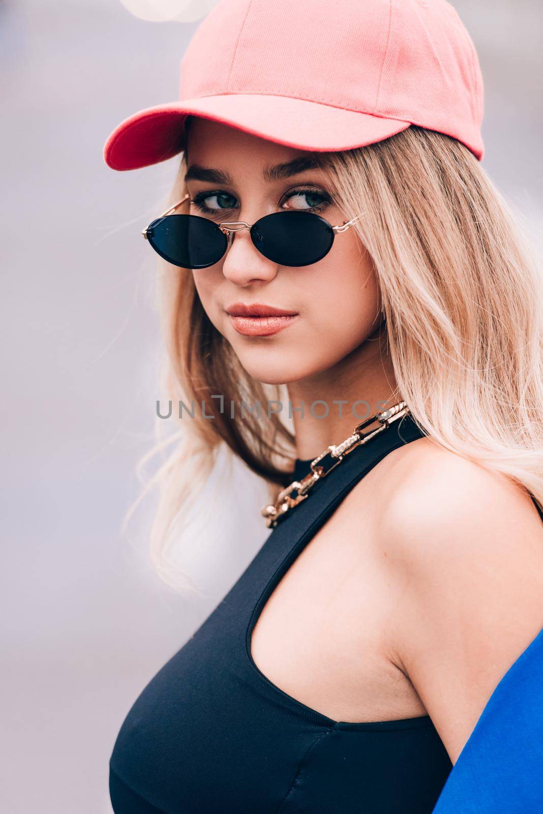 Young sexy blonde hipster woman posing on the street. Wearing blue stylish jacket, jeans and baseball hat and sunglasses. by Ashtray25