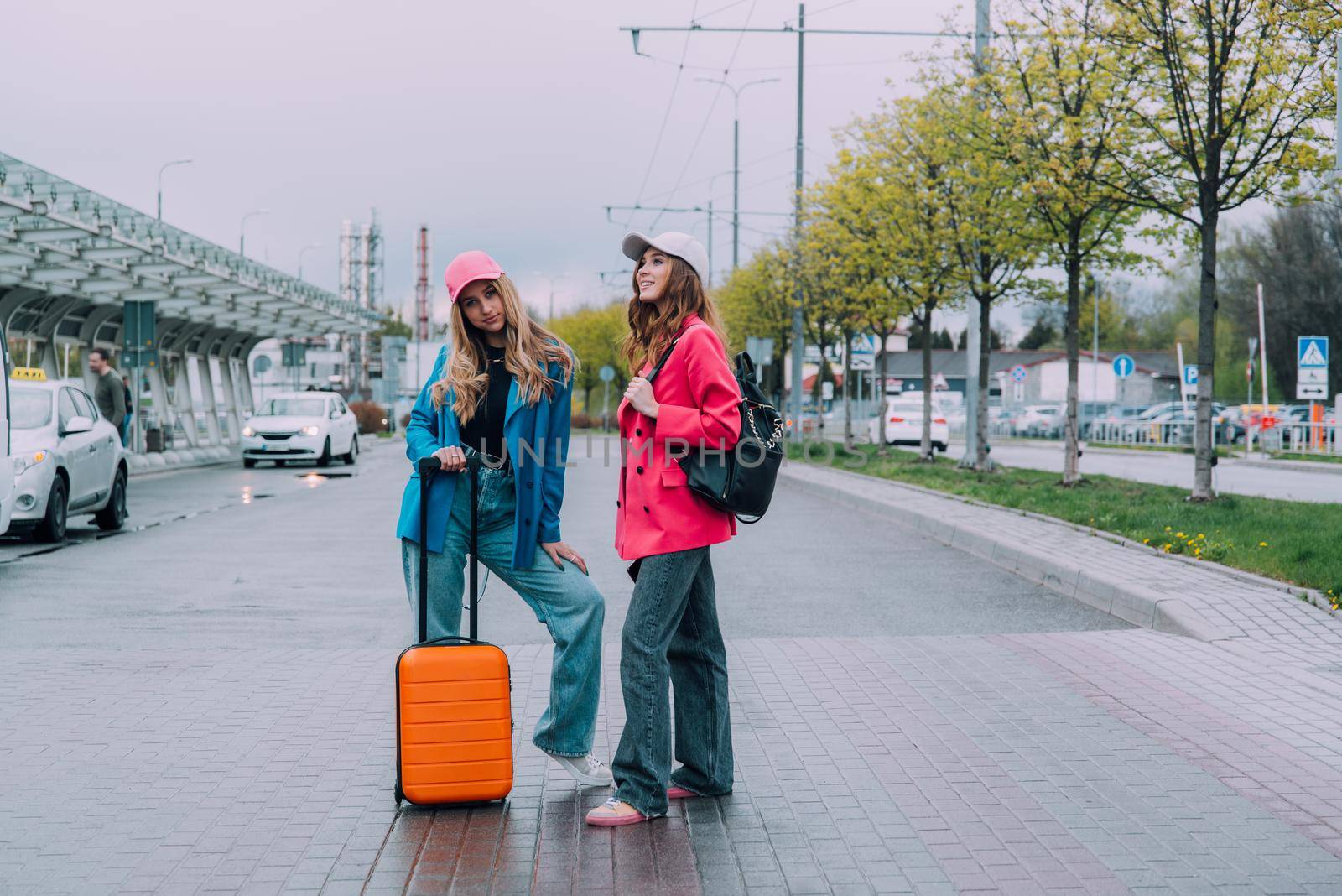 Two happy girls walking near airport, with luggage. Air travel, summer holiday by Ashtray25