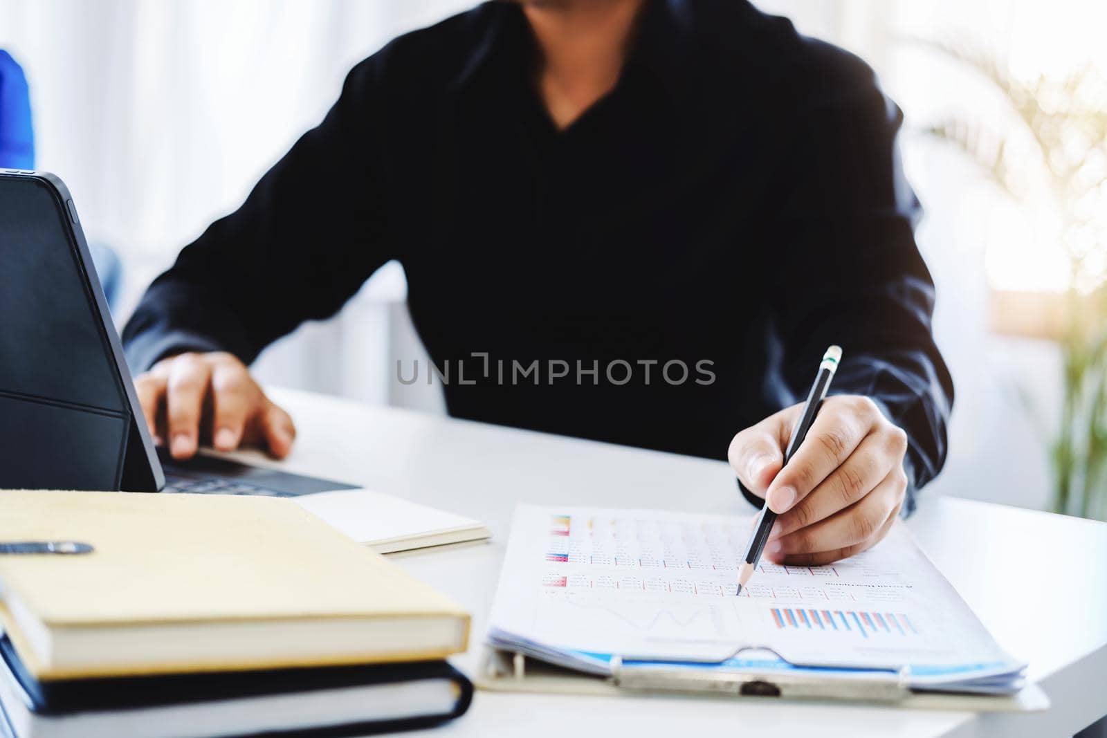 An accountant, businessman, auditor, economist man holding a pen pointing to a budget document and using tablet to examine and assess financial and investment risks for a company