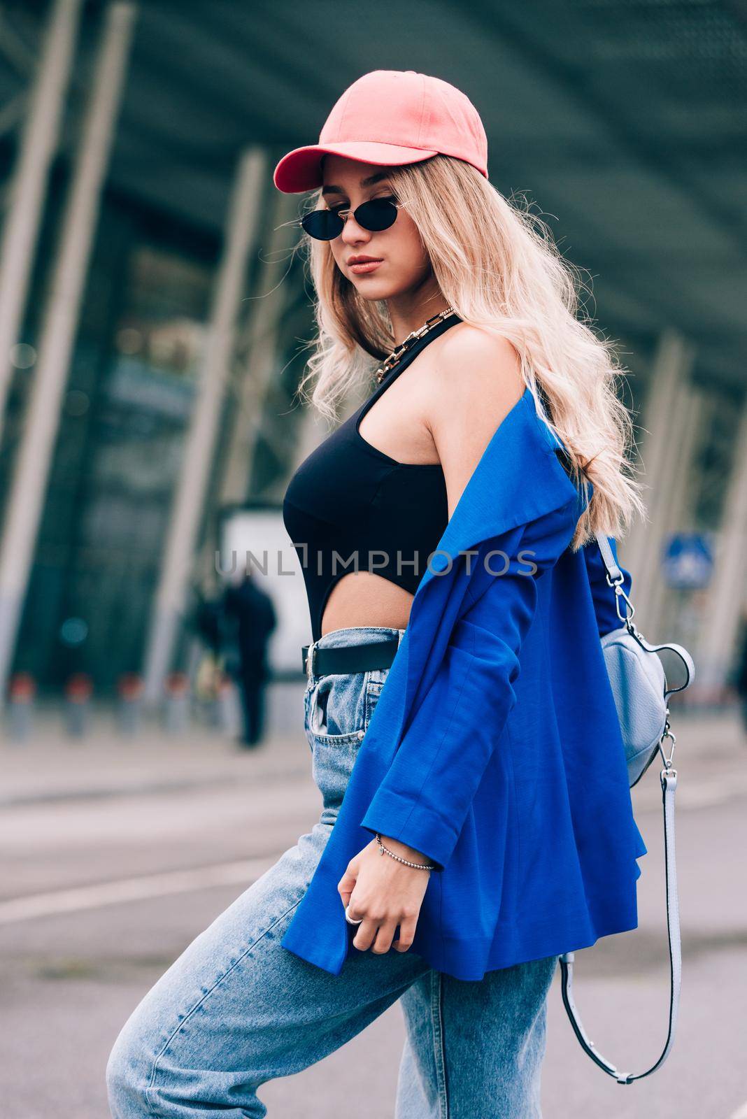 Young sexy blonde hipster woman posing on the street. Wearing blue stylish jacket, jeans and baseball hat and sunglasses. by Ashtray25