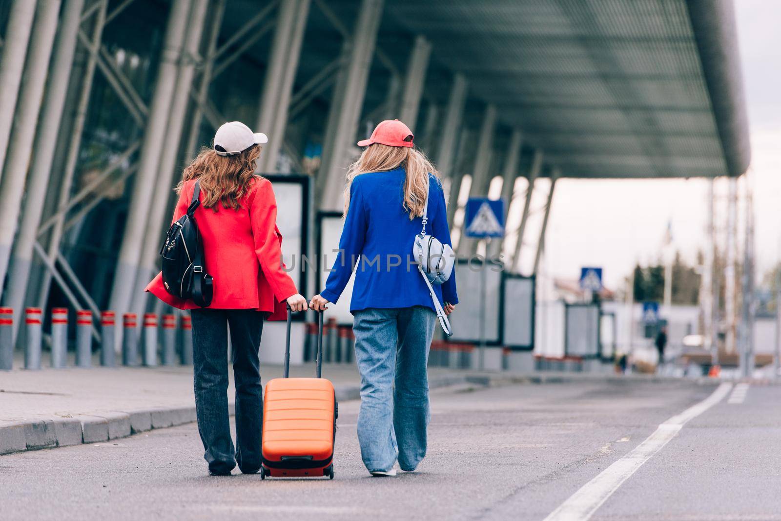 Two happy girls walking near airport, with luggage. Air travel, summer holiday. View from the back