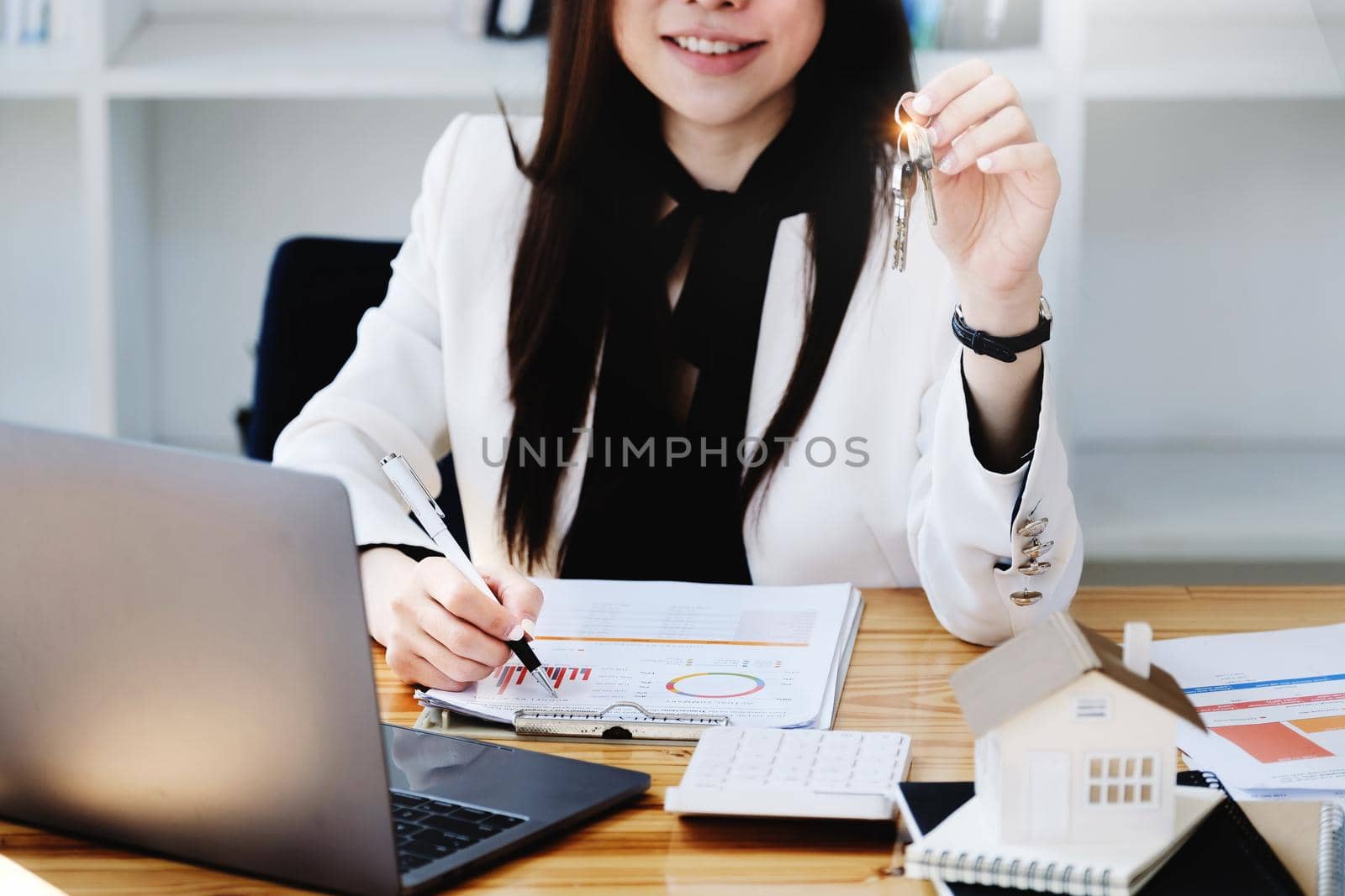 Asian woman accountant, business woman, real estate agent, holding a pen, pointing at home loan and interest documents to calculate the risk in the home investment budget. by Manastrong