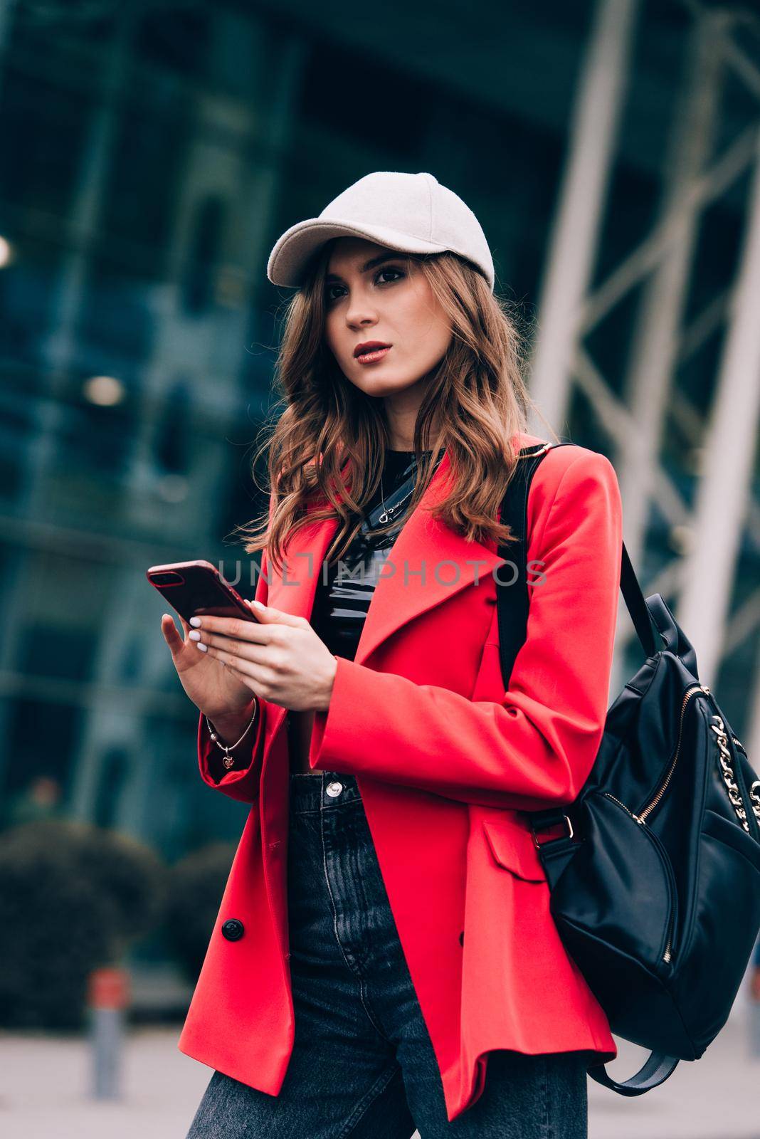 Stylish woman on the street uses a mobile phone. online shopping. use of mobile applications. beautiful woman with long dark hair in a red jacket, black top and a cap