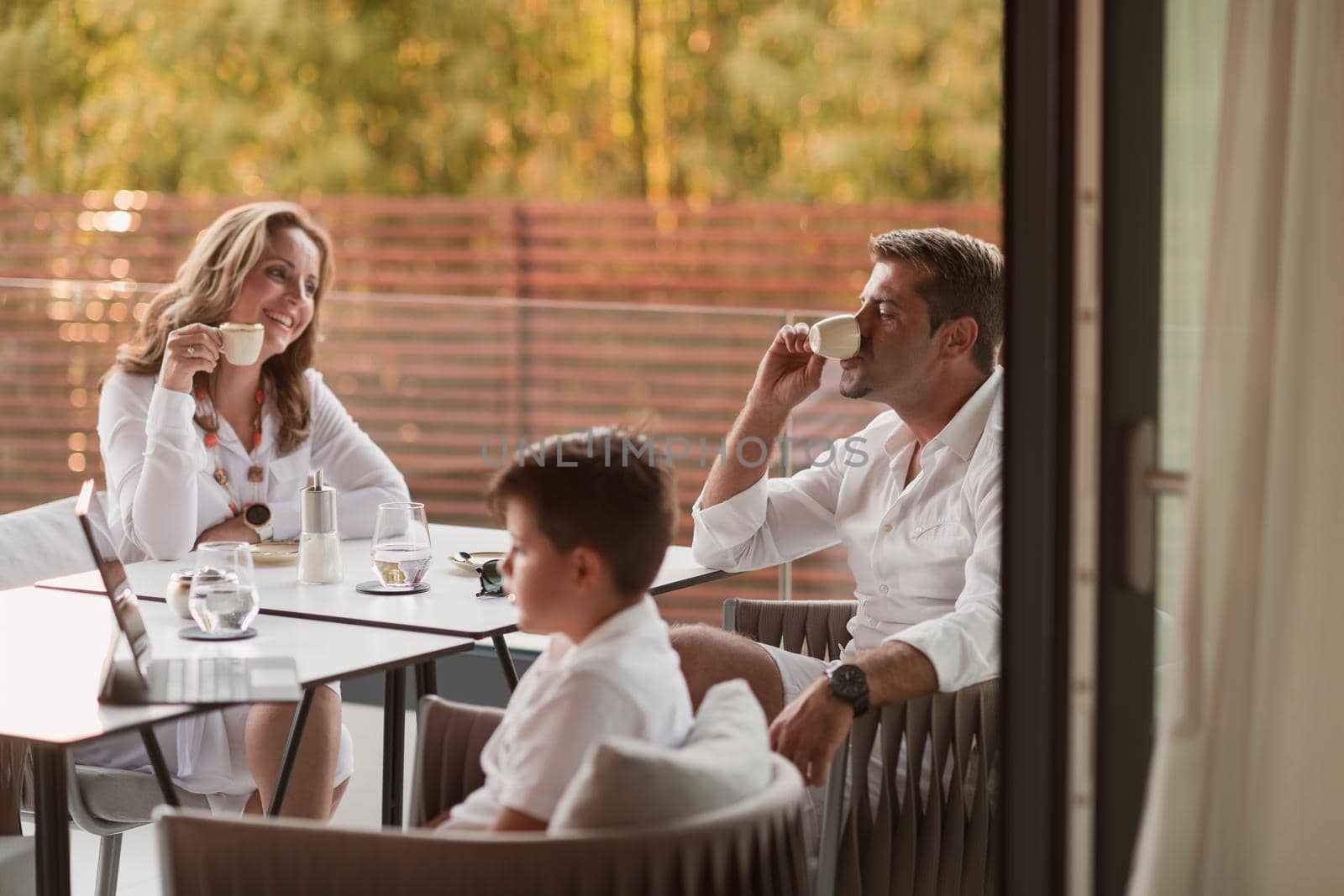 An elderly couple enjoys the terrace of a luxury house with their son during the holidays. Selective focus by dotshock