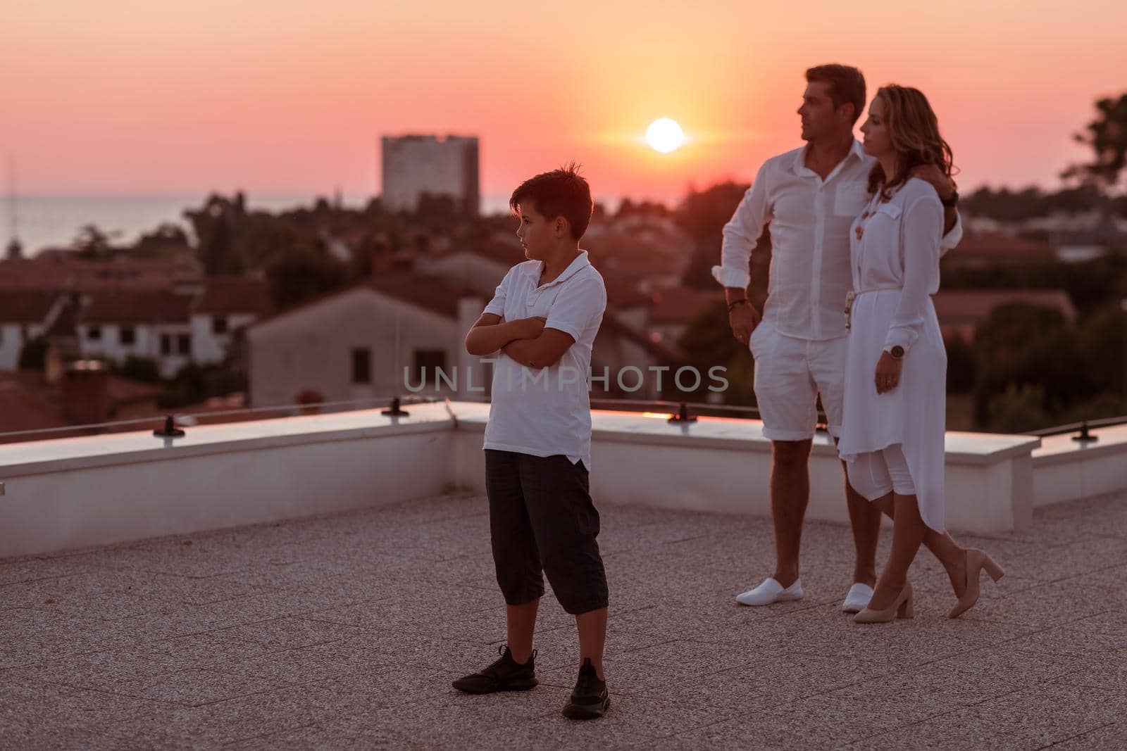 Happy family enjoys and spends time together on the roof of the house while watching the sunset on the open sea together by dotshock