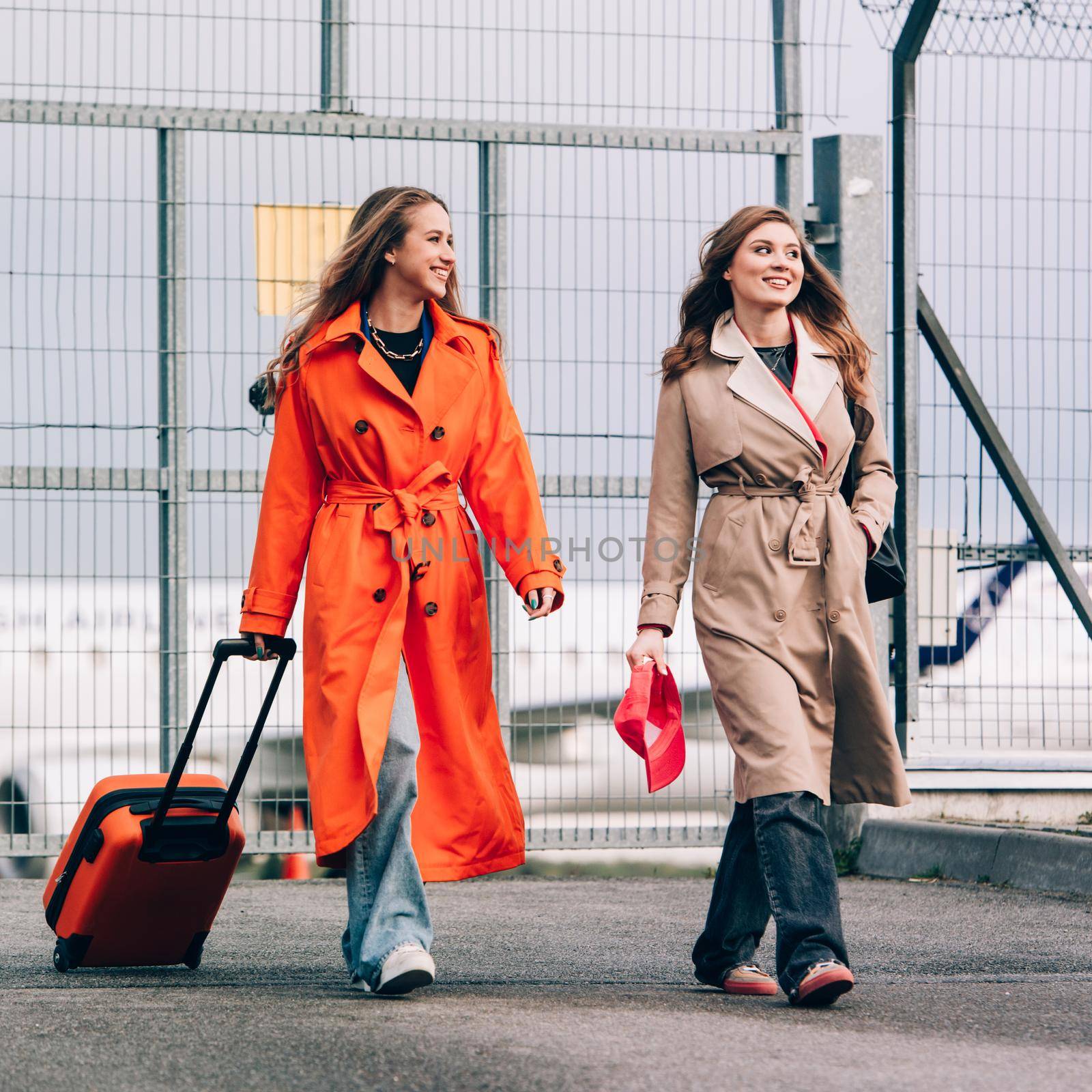 Two happy girls walking near airport, with luggage. Air travel, summer holiday by Ashtray25