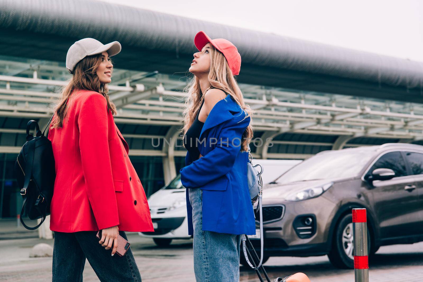 Two happy girls walking near airport, with luggage. Air travel, summer holiday.