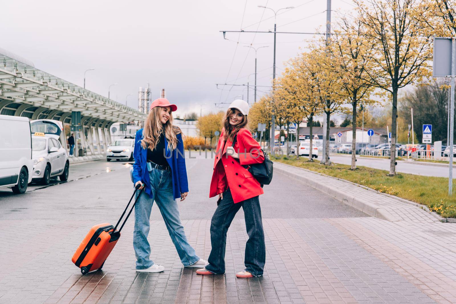 Two happy girls walking near airport, with luggage. Air travel, summer holiday.