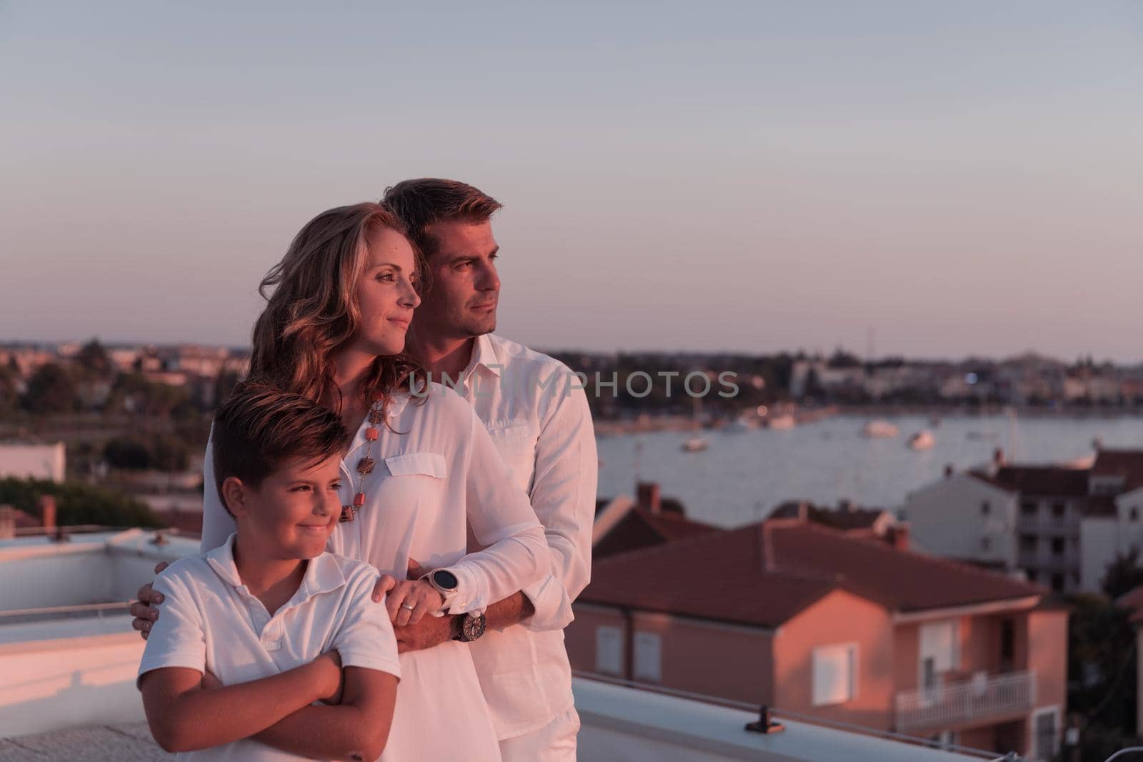 The happy family enjoys and spends time together on the roof of the house while watching the sunset on the open sea together. High-quality photo