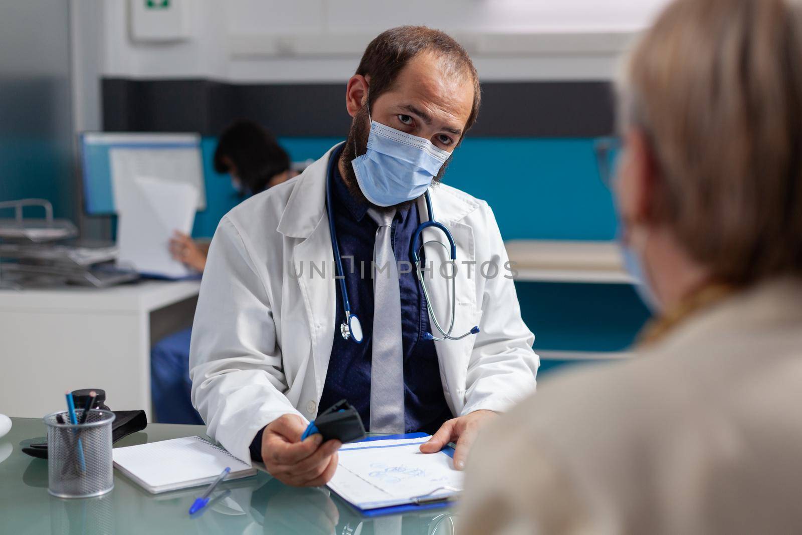 Doctor putting medical seal on prescription paper, giving medicine to senior patient at examination. General practitioner using stamp on consultation report during covid 19 pandemic.