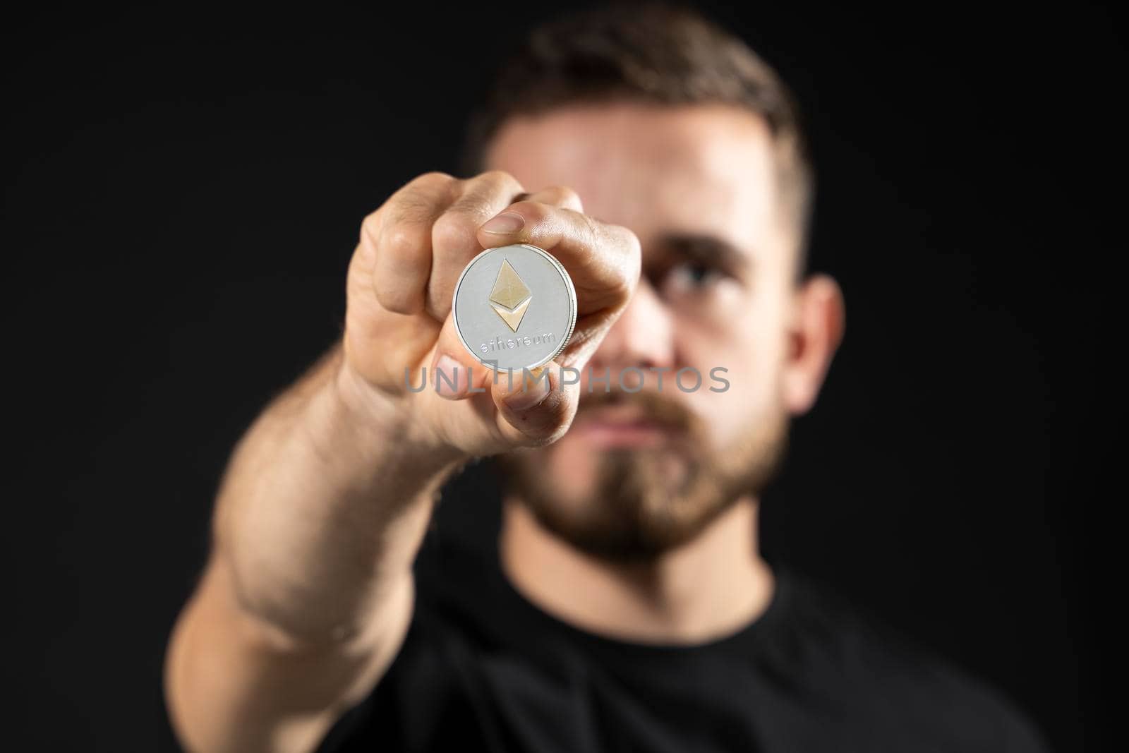 Successful business man in black t-shirt with ethereum coin isolated on grey background in studio. Hold ethereum, bitcoin, future currency. by vovsht