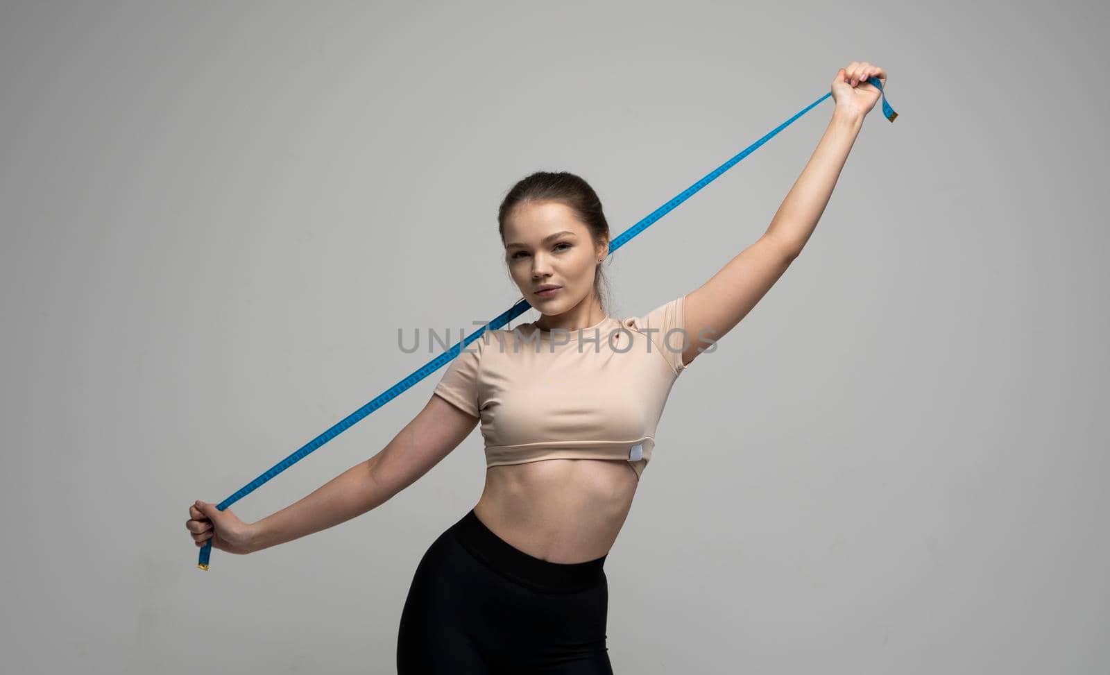 Attractive brunette woman in sportswear holding a blue measuring tape. Weight loss and diet concepts. Health care and healthy nutrition. Perfect slim body. by vovsht