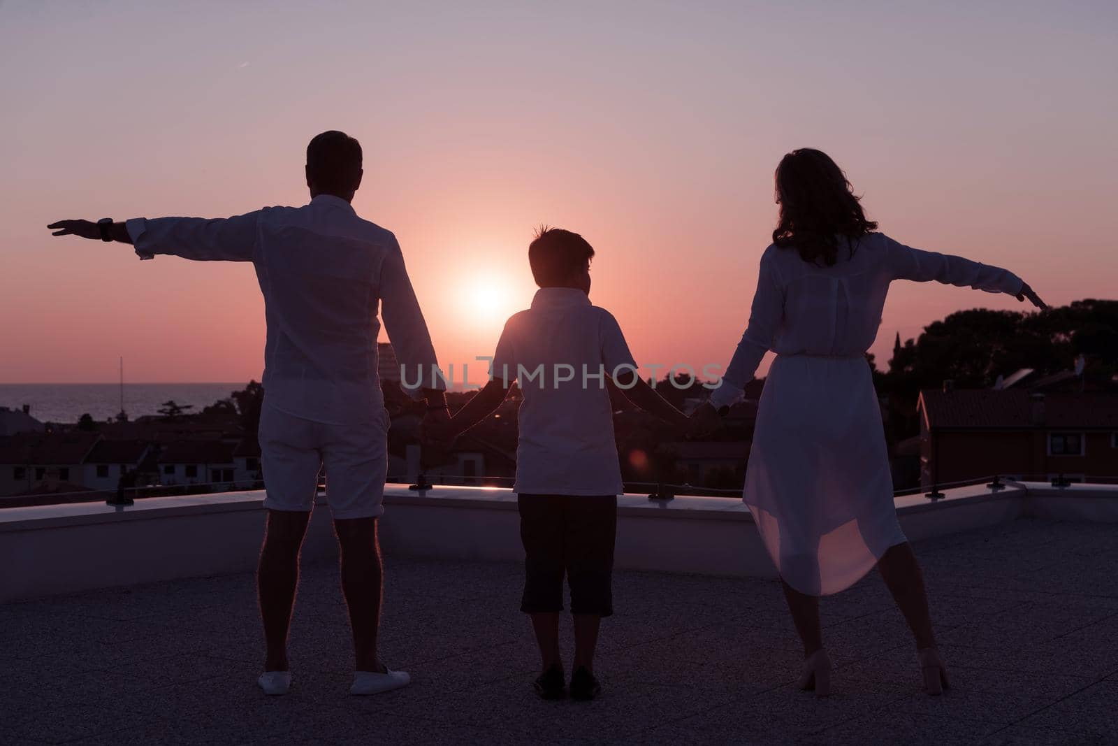 The happy family enjoys and spends time together on the roof of the house while watching the sunset on the open sea together. High-quality photo