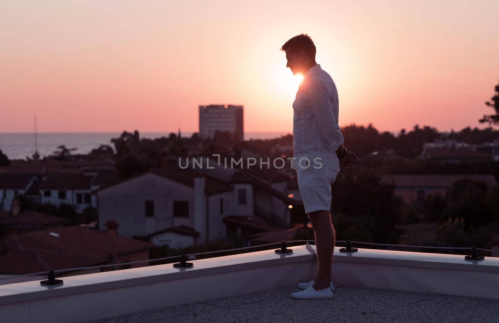 an elderly businessman in casual clothes enjoys the roof of his house at sunset time. Selective focus. High-quality photo