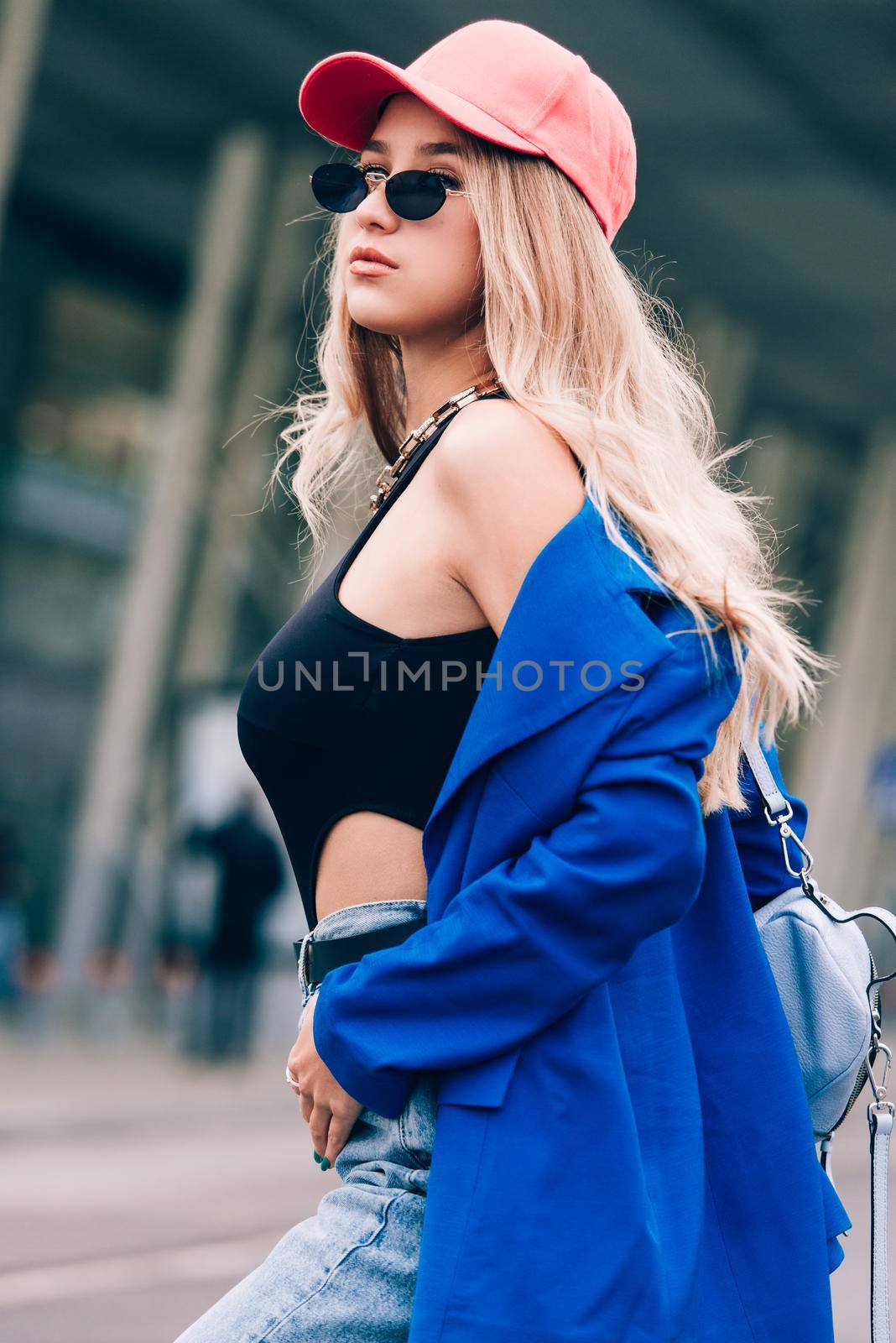 Young sexy blonde hipster woman posing on the street. Wearing blue stylish jacket, jeans and baseball hat and sunglasses. by Ashtray25