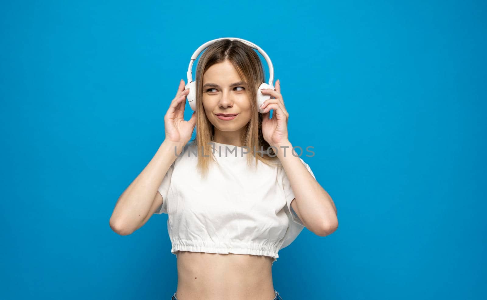 Beautiful young woman in headphones listening to music blue background. Young beautiful woman in bright outfit enjoying a music