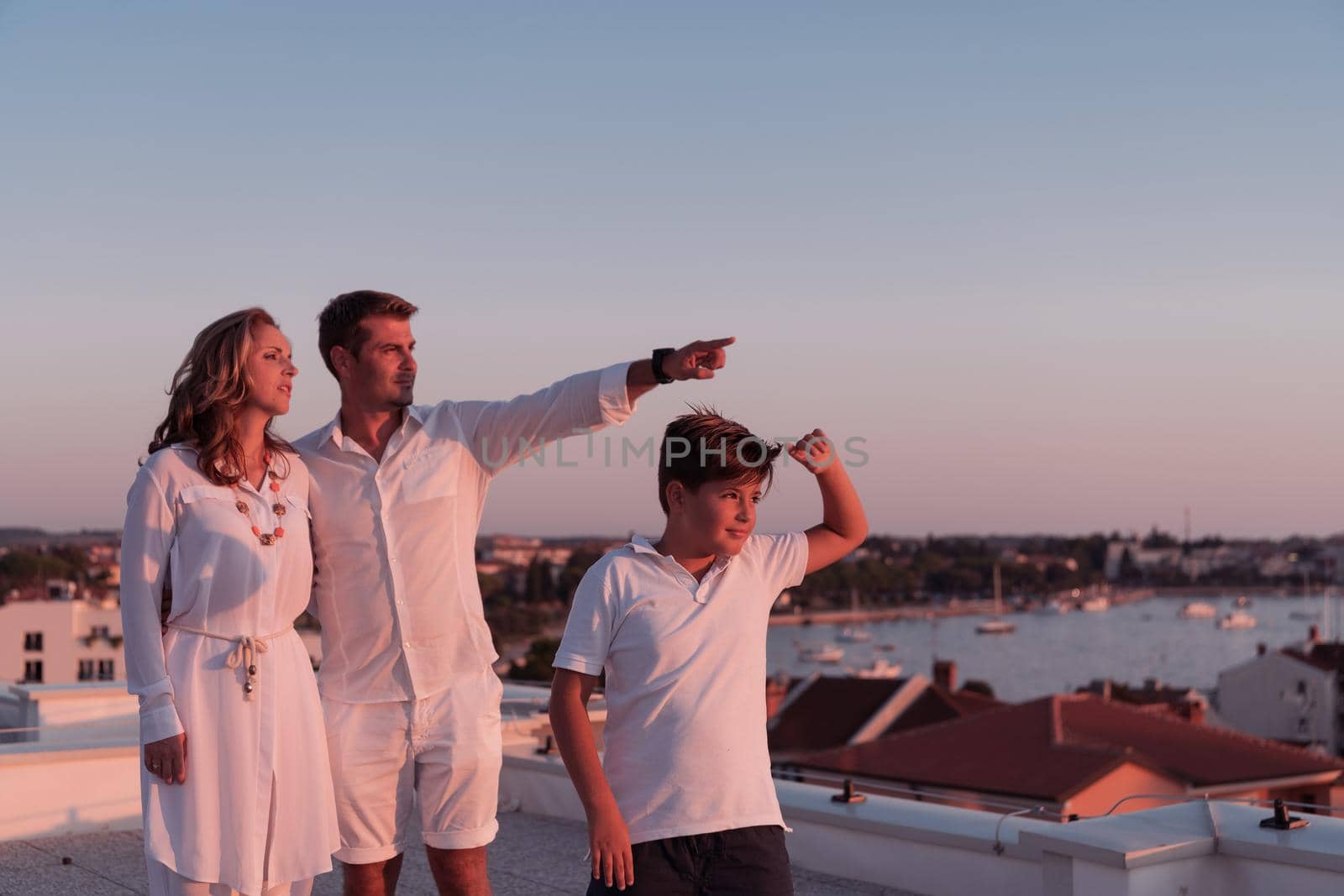 The happy family enjoys and spends time together on the roof of the house while watching the sunset on the open sea together. High-quality photo