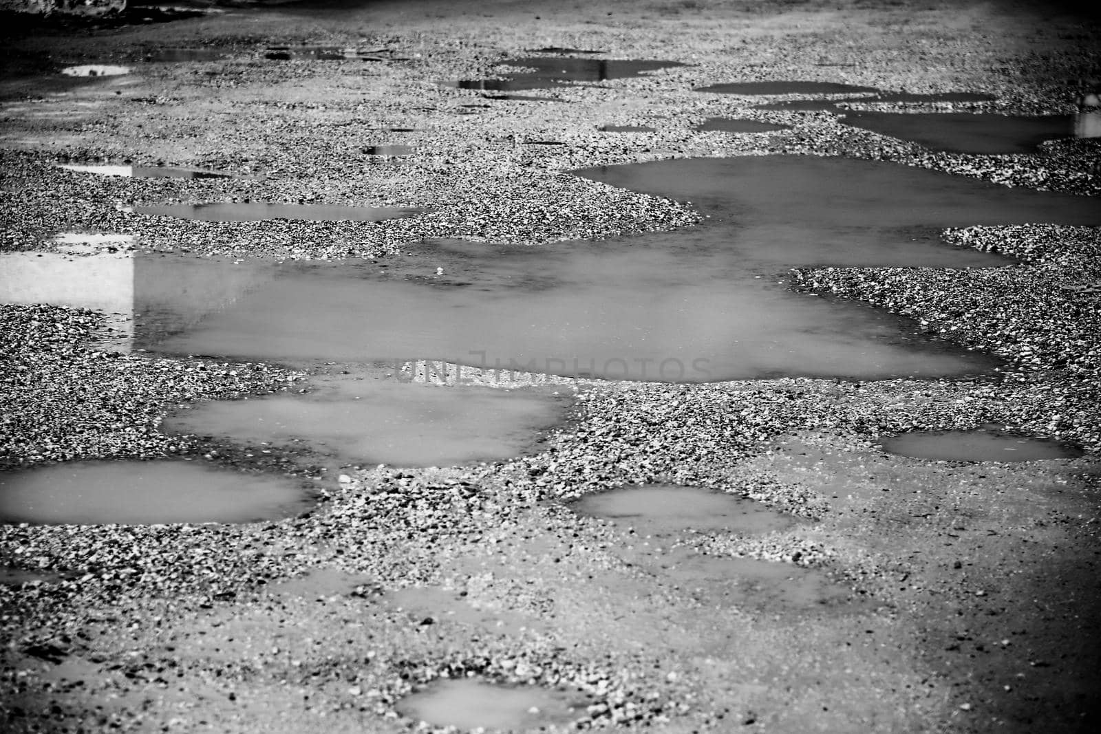 Bumpy gravel ground covered by rainwater. Monochrome picture.