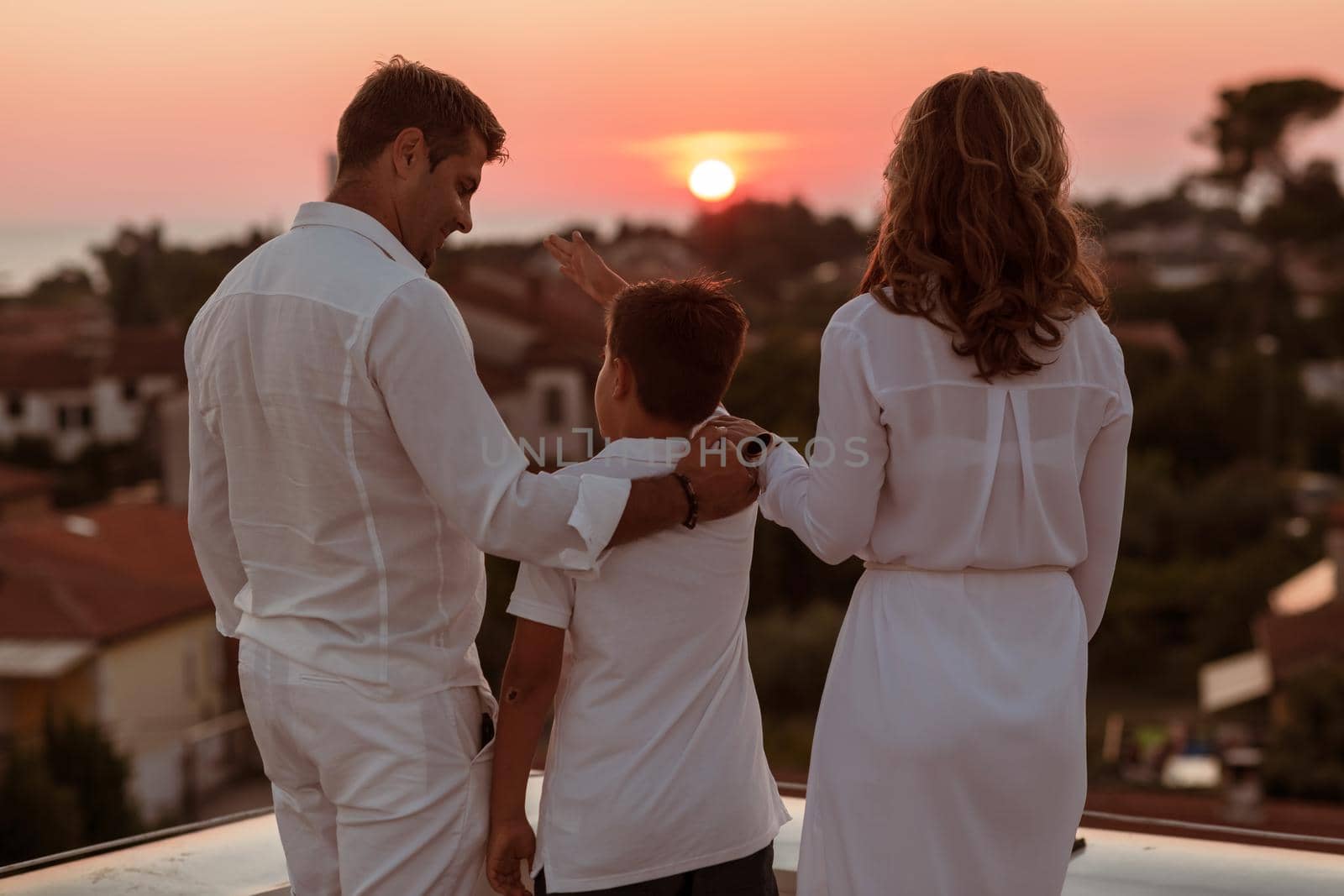 Happy family enjoys and spends time together on the roof of the house while watching the sunset on the open sea together by dotshock