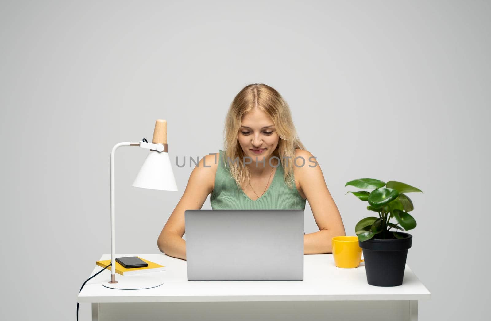 Portrait of a pretty young woman studying while sitting at the table with grey laptop computer, notebook. Smiling business woman working with a laptop isolated on a grey background. by vovsht