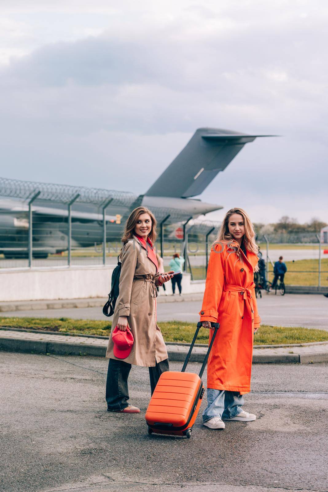 Two happy girls walking near airport, with luggage. Air travel, summer holiday by Ashtray25